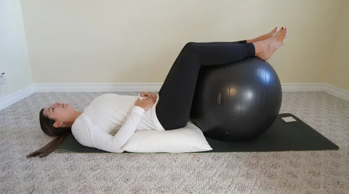 Laura lying on her back on a yoga mat with a pillow under her knees, practicing pelvic floor relaxation